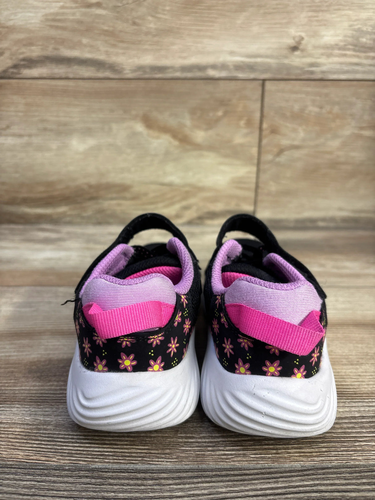 Rear view of Skechers Ultra Flex toddler sneakers, size 11C, showing pink floral print, pink pull tab, and white wavy soles on wood floor