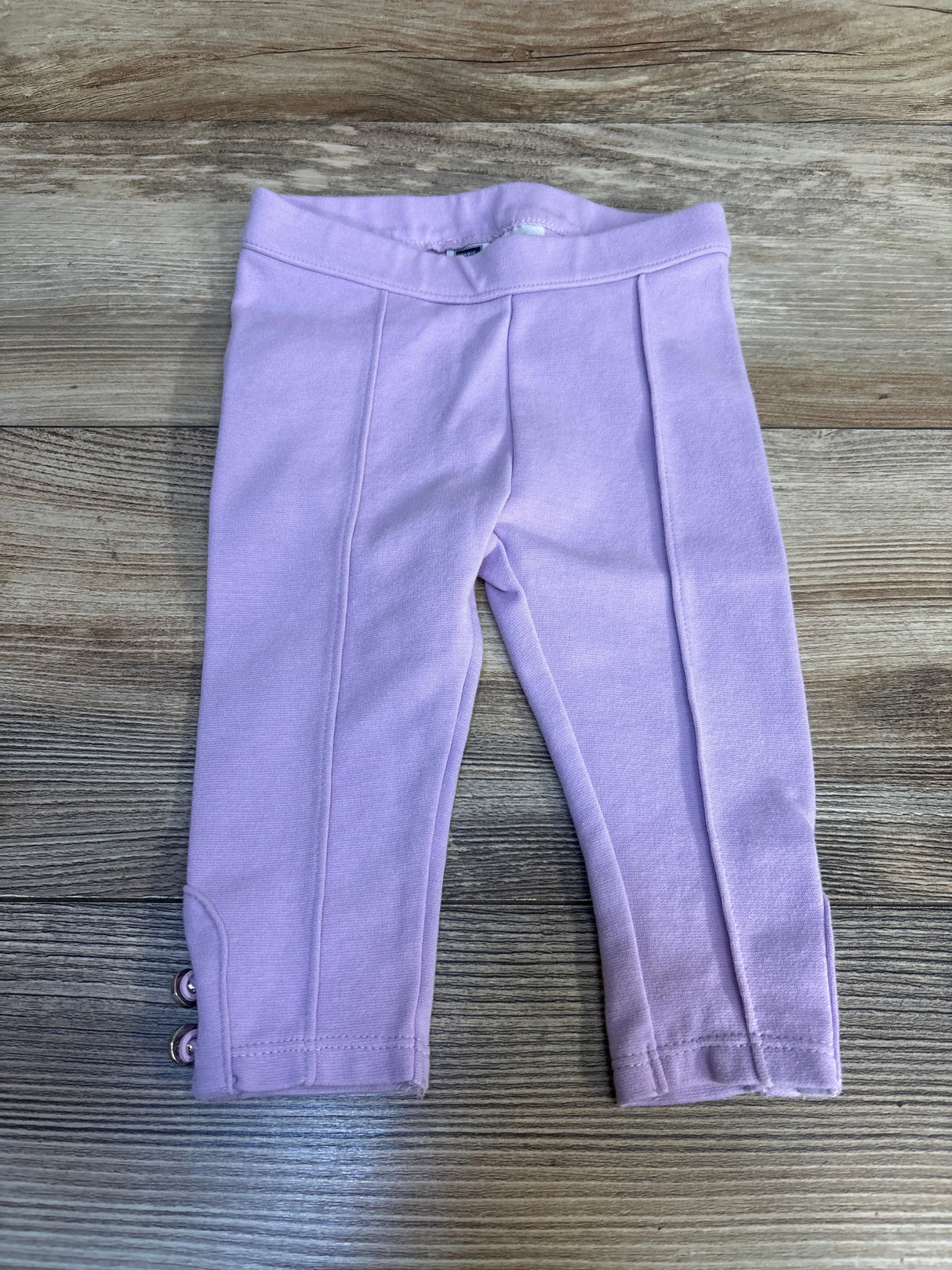 Light purple baby leggings with front seams and button accents, displayed on wood background