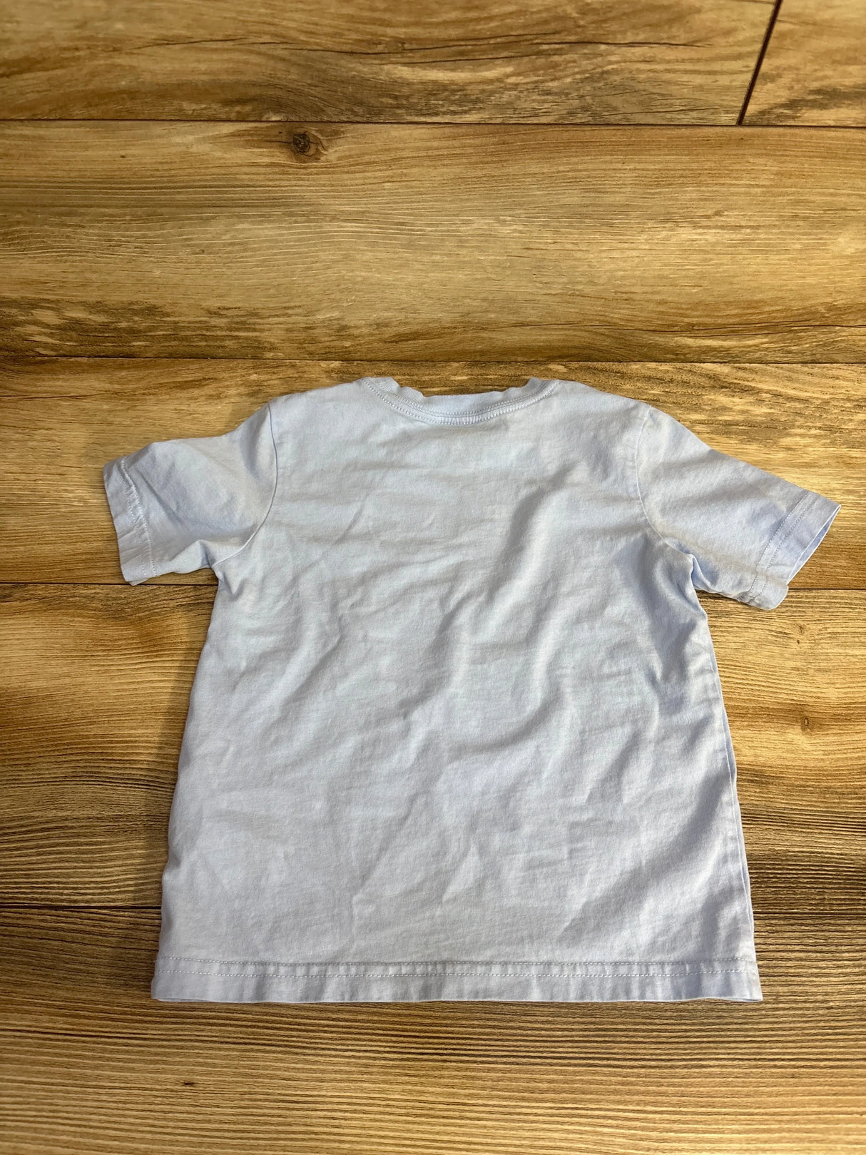Back view of plain light blue short sleeve kids t-shirt on wooden floor