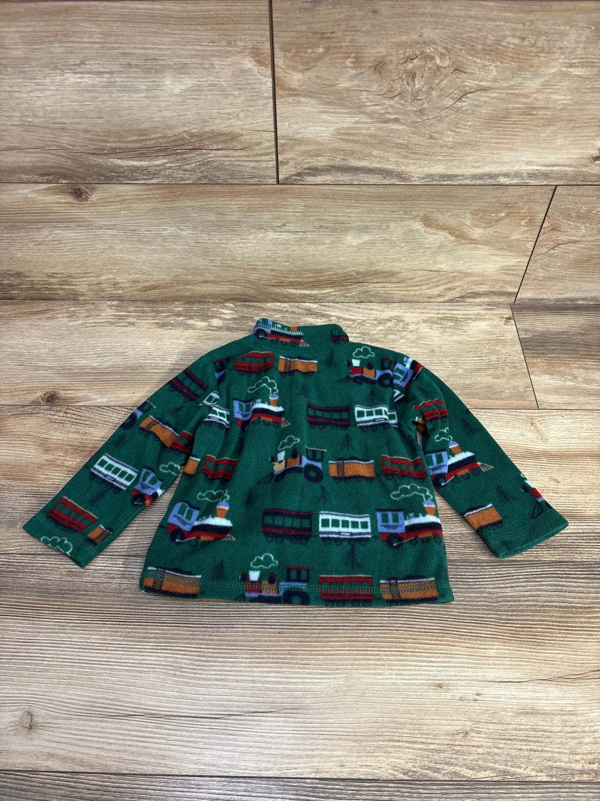 Green fleece toddler jacket with colorful train print on wooden floor