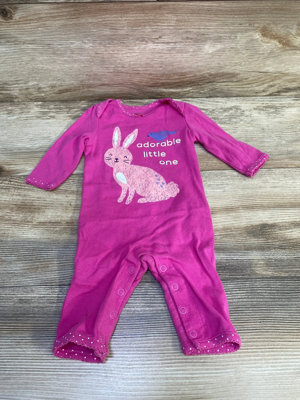 Front of Carter's pink long-sleeve baby coverall with bunny graphic, adorable little one text, and leg snaps on wood background