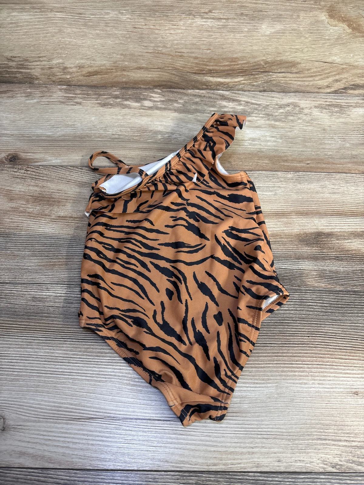 Top view of Carter’s one-piece swimsuit showcasing brown tiger-stripe pattern and shoulder straps with a wood-grain background