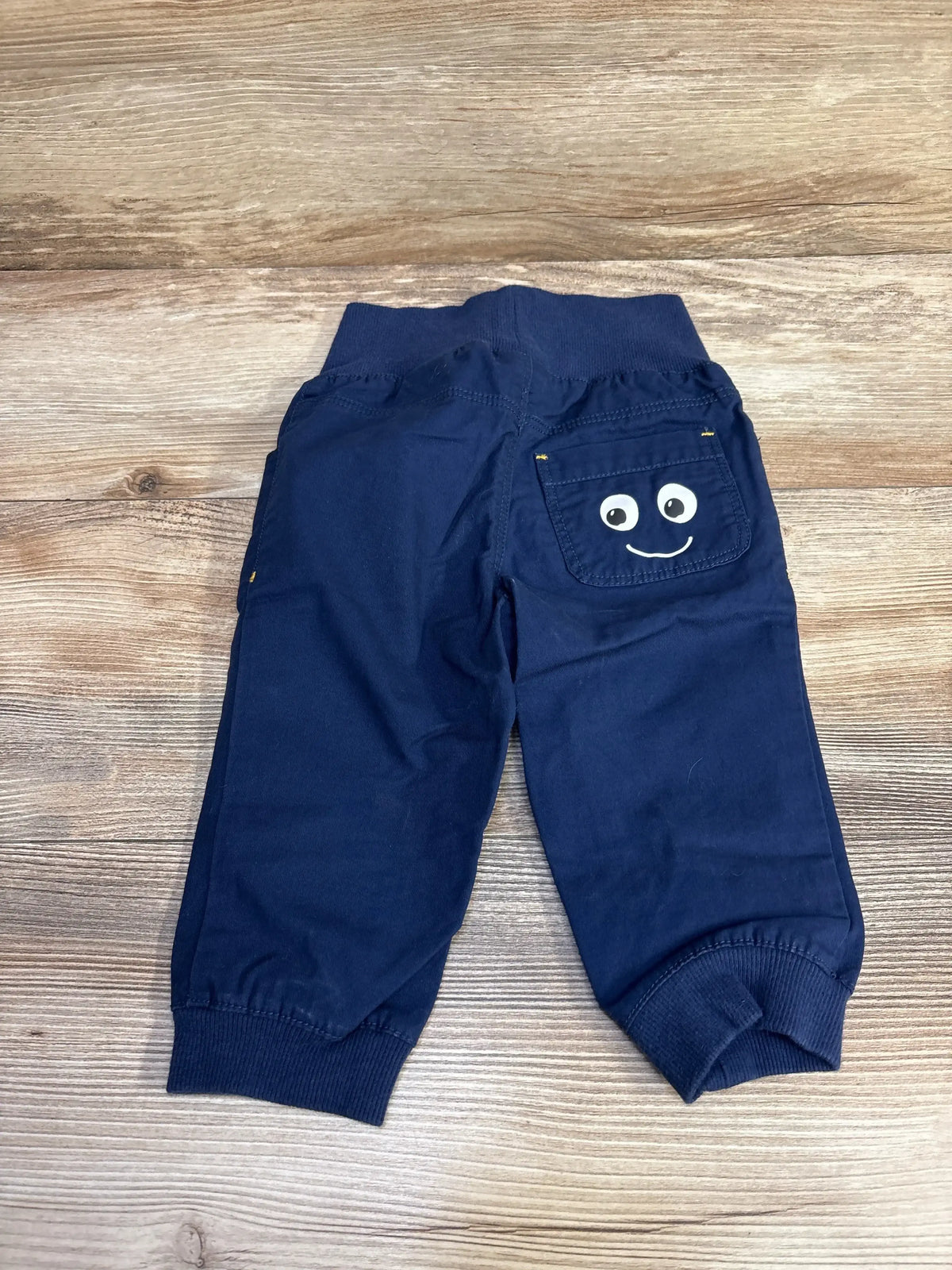 Back view of navy H&M pull-on jogger pants with elastic waistband, cuffs, and back pocket with smiling face on wood
