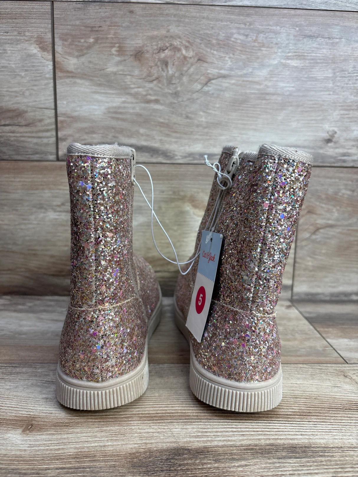 Pair of glittery pink toddler boots with a size tag, displayed on wood floor