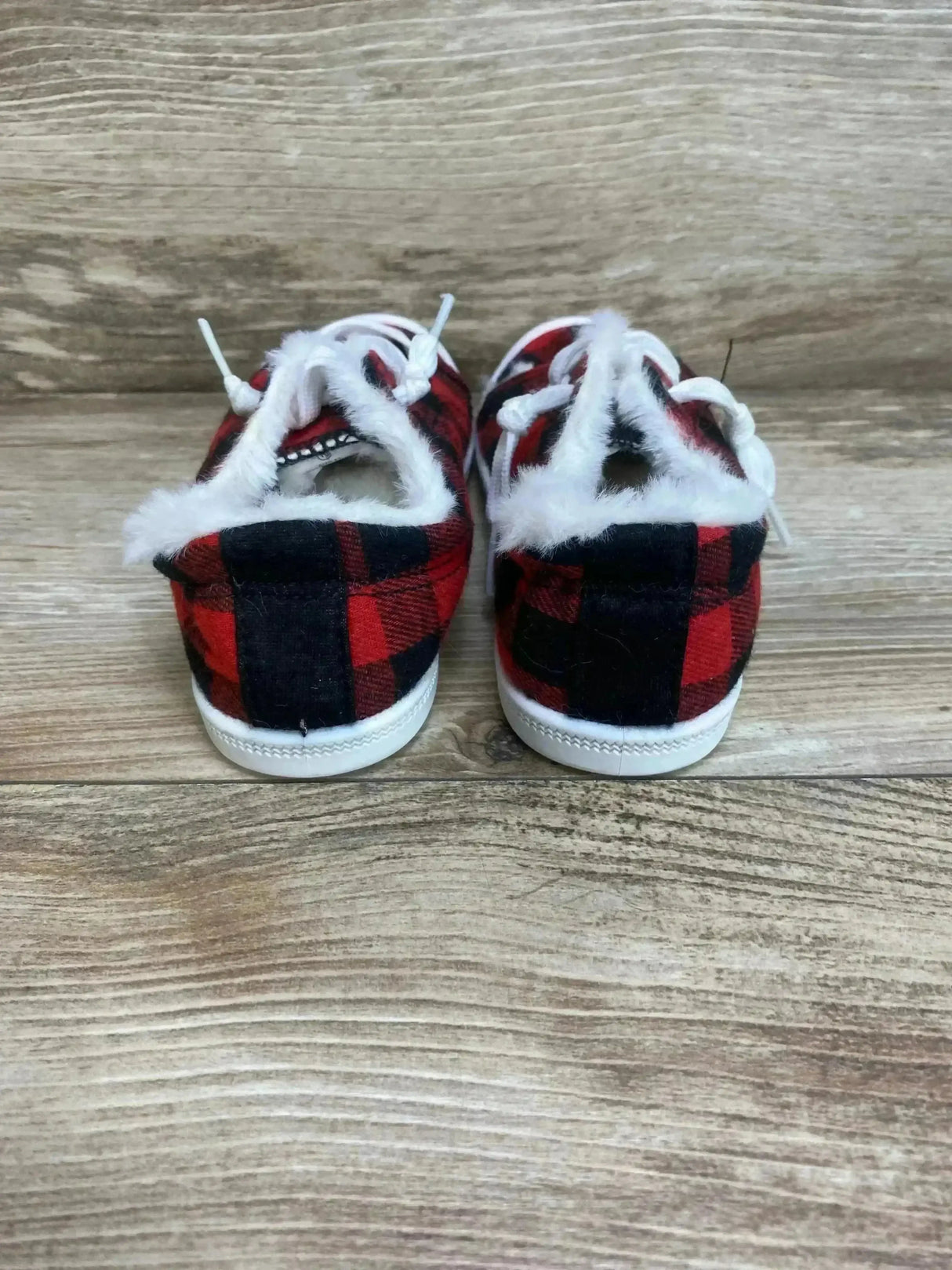 Rear view of toddler slip-on sneakers size 10C showcasing red and black buffalo plaid fabric and white faux-fur lining on a wood floor