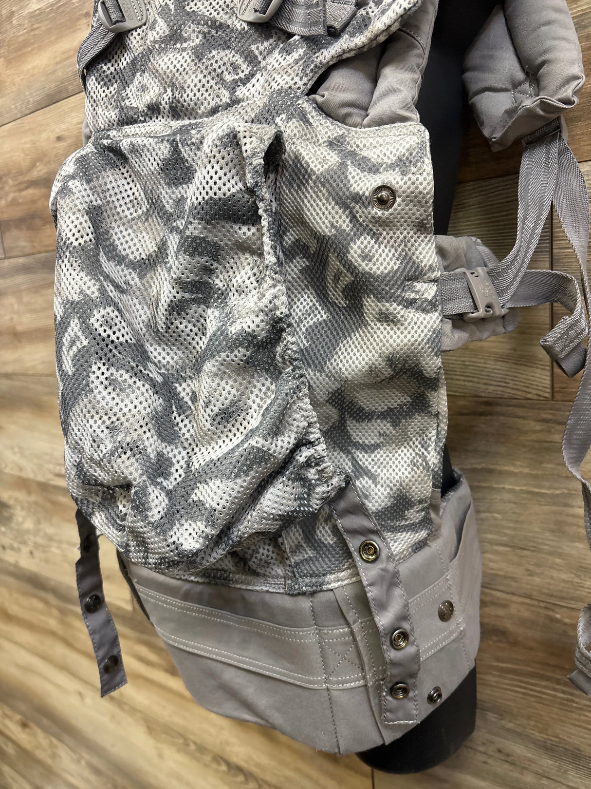Gray mesh baby carrier with buckles and snap buttons on wood background