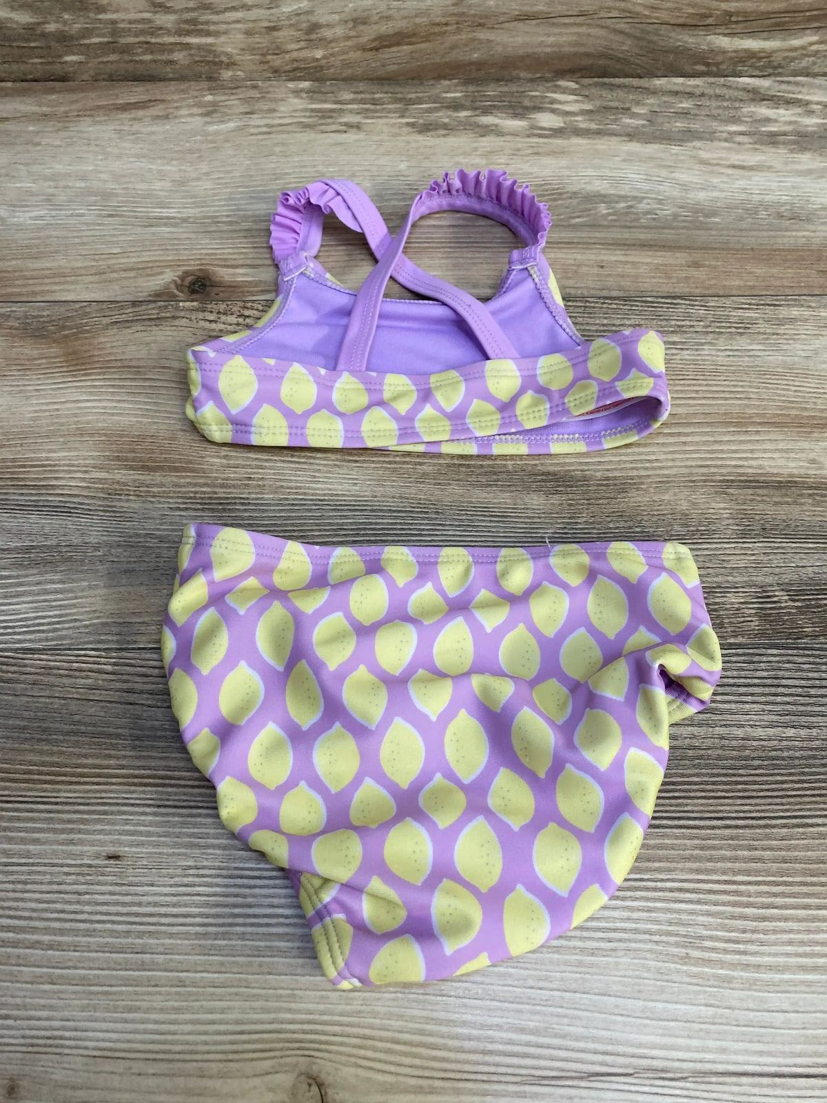 Flat lay of Cat and Jack 2pc lemon print swimsuit in purple with yellow lemon print and ruffled straps on wood plank floor