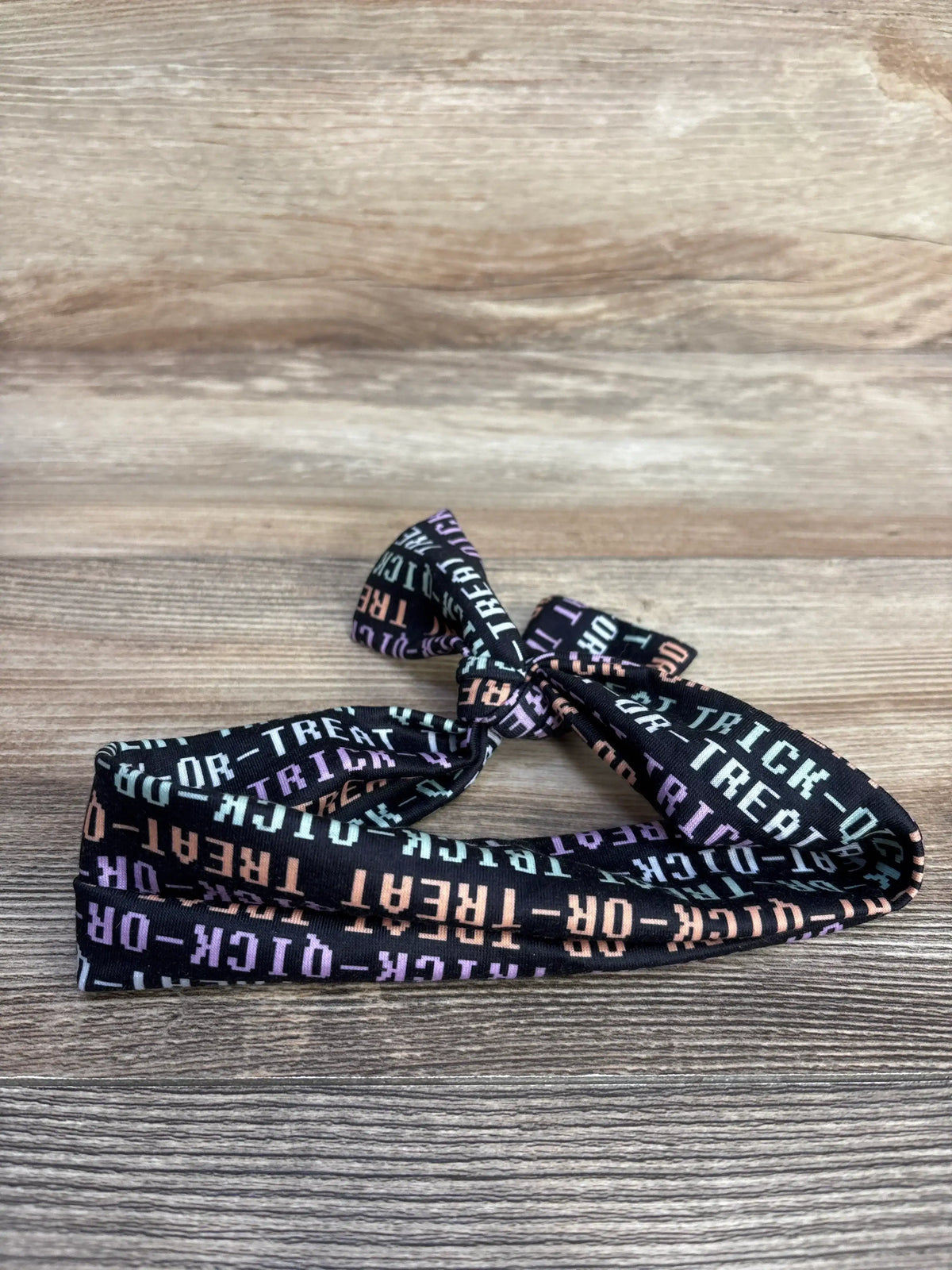 Close-up of Halloween headwrap showcasing a tied bow and colorful Trick or Treat lettering on black fabric with wood background