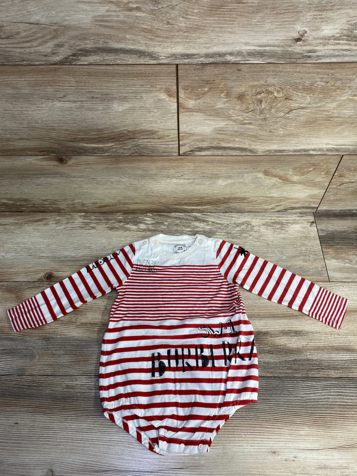Red and white striped Burberry baby romper with long sleeves and snap buttons on wooden floor