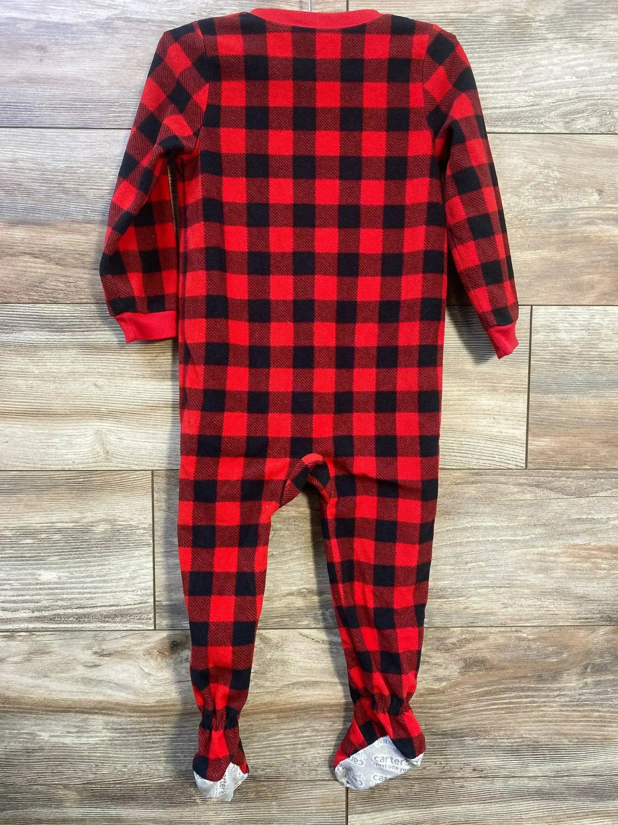 Back view of red and black buffalo-check footed blanket sleeper for toddler showing long sleeves and fleece texture on wooden floor