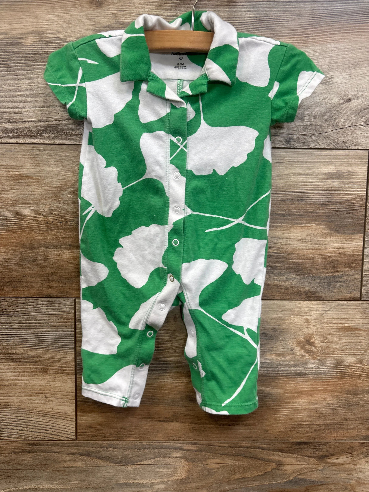 Green and white short sleeve baby romper with leaf pattern, laid flat on wood background