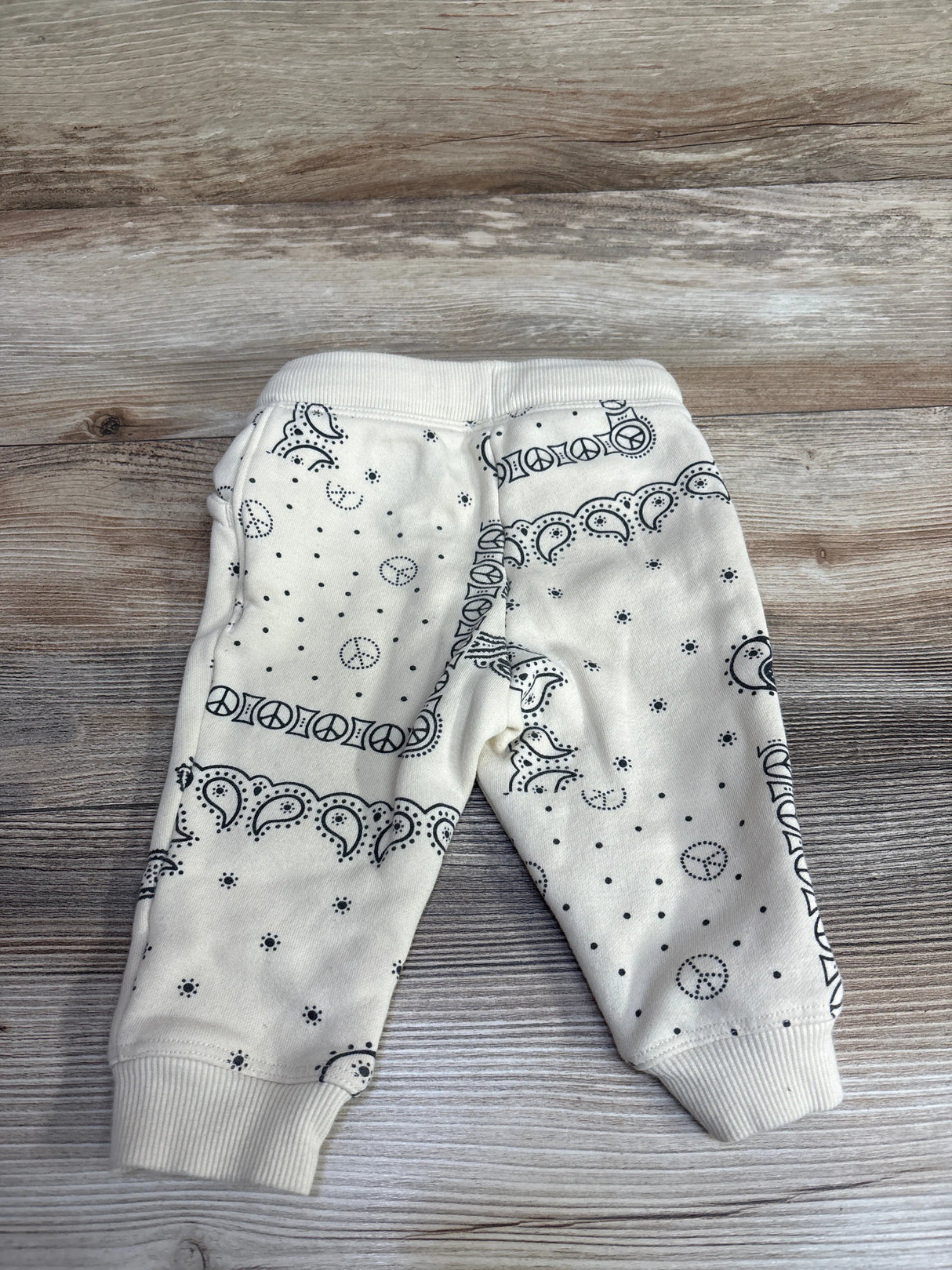 White baby pants with black peace sign and paisley pattern on wooden floor
