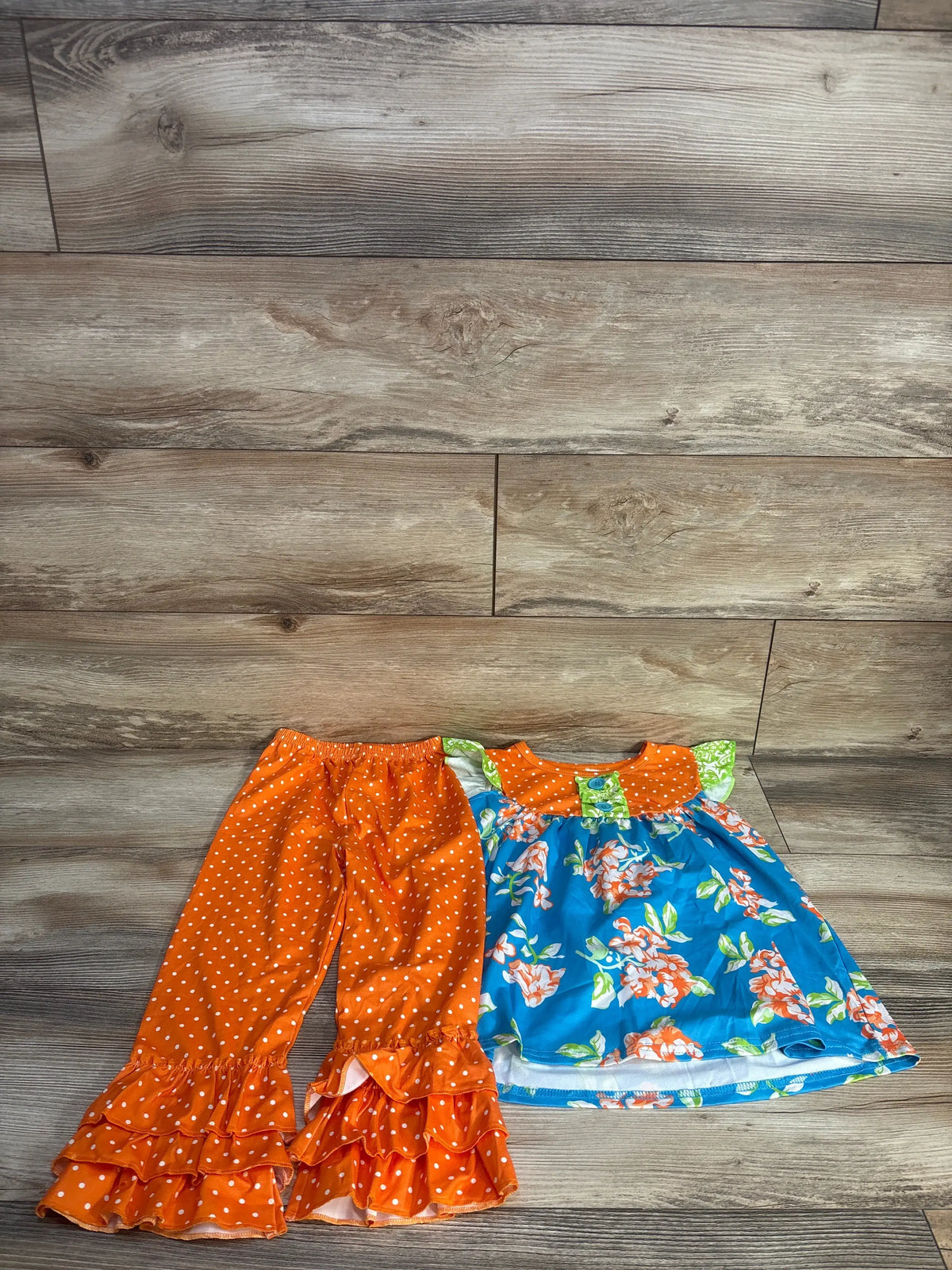 Front view of Waverly Scarlet toddler dress and ruffle pants set showcasing orange polka-dot ruffles and blue floral dress on a wood floor