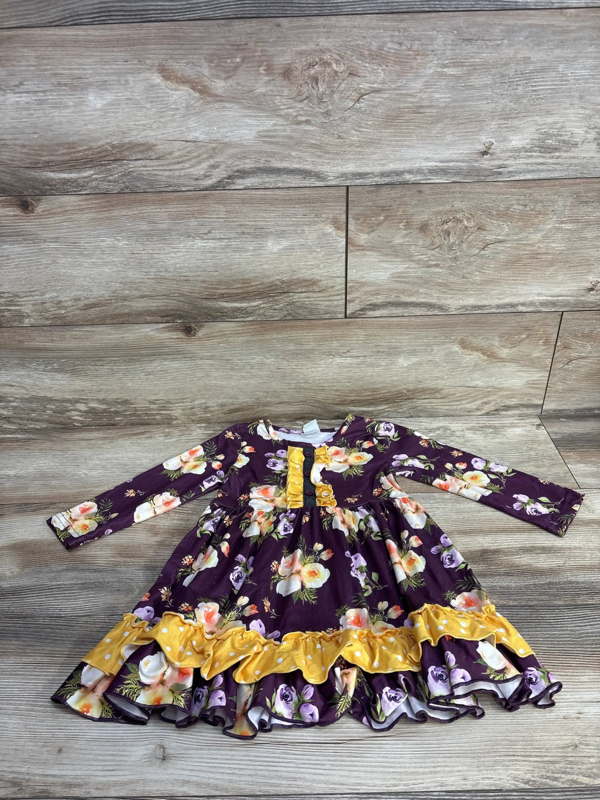 Long-sleeve toddler dress with purple floral pattern and yellow ruffled accents on wooden floor