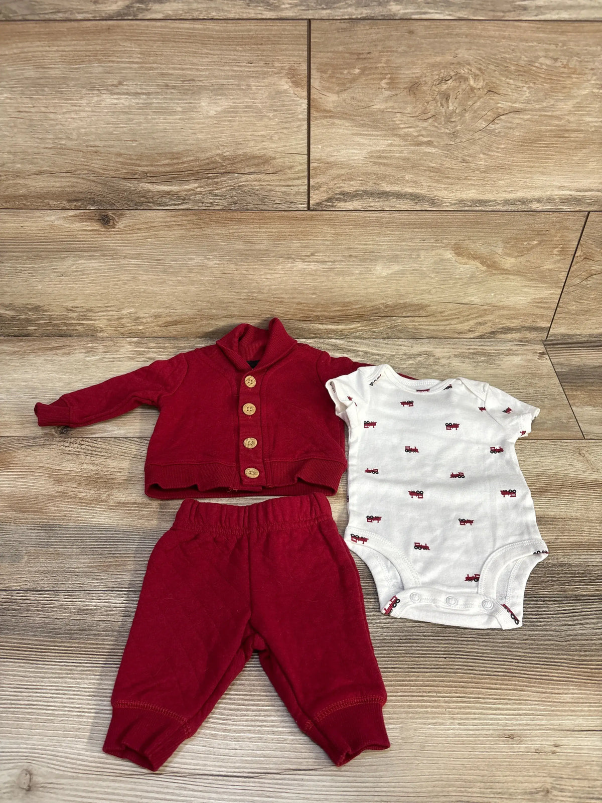 Front view of Carter’s newborn set showcasing a red quilted jacket, matching pants, and patterned bodysuit on wood