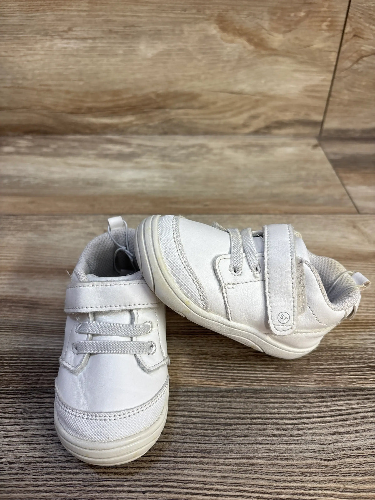 Front and side views of Stride Rite Taye 2.0 sneaker in white showing elastic laces and hook-and-loop straps on a wood floor