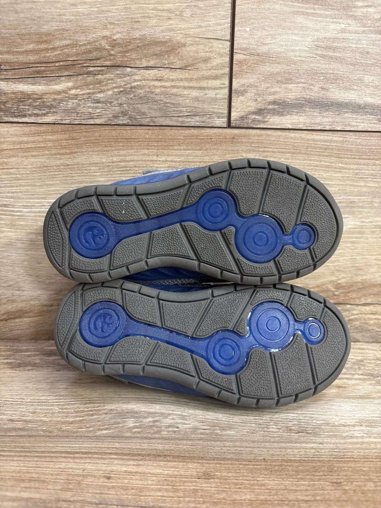 Bottom view of blue and gray children's shoes showing rubber soles with circular blue accents on wooden floor