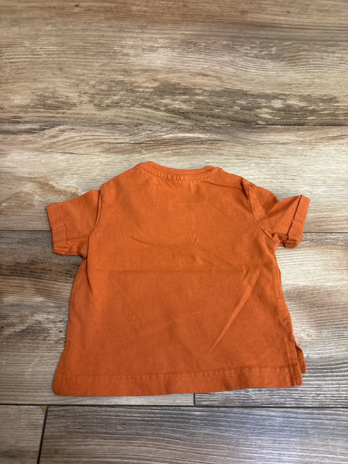 Back view of newborn Rust Baby Berry Straya short-sleeve shirt showing plain back on wood floor