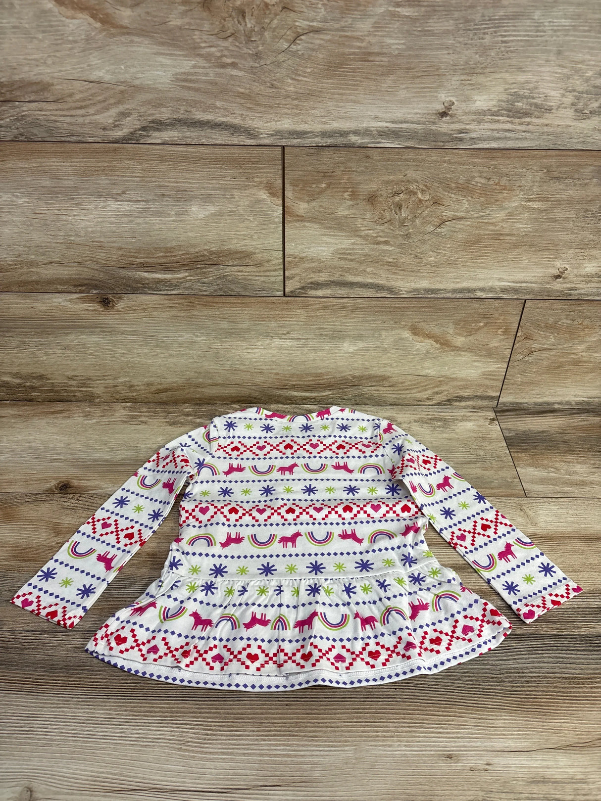 Long sleeve white toddler top with colorful unicorn, rainbow, heart, and star patterns on wood floor