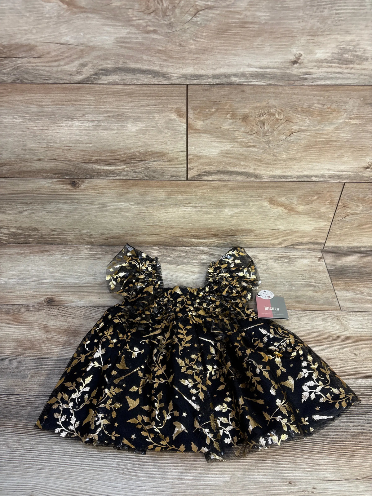 Front view of Elphaba-inspired toddler dress with black and gold pattern and ruffle sleeves on wood flooring