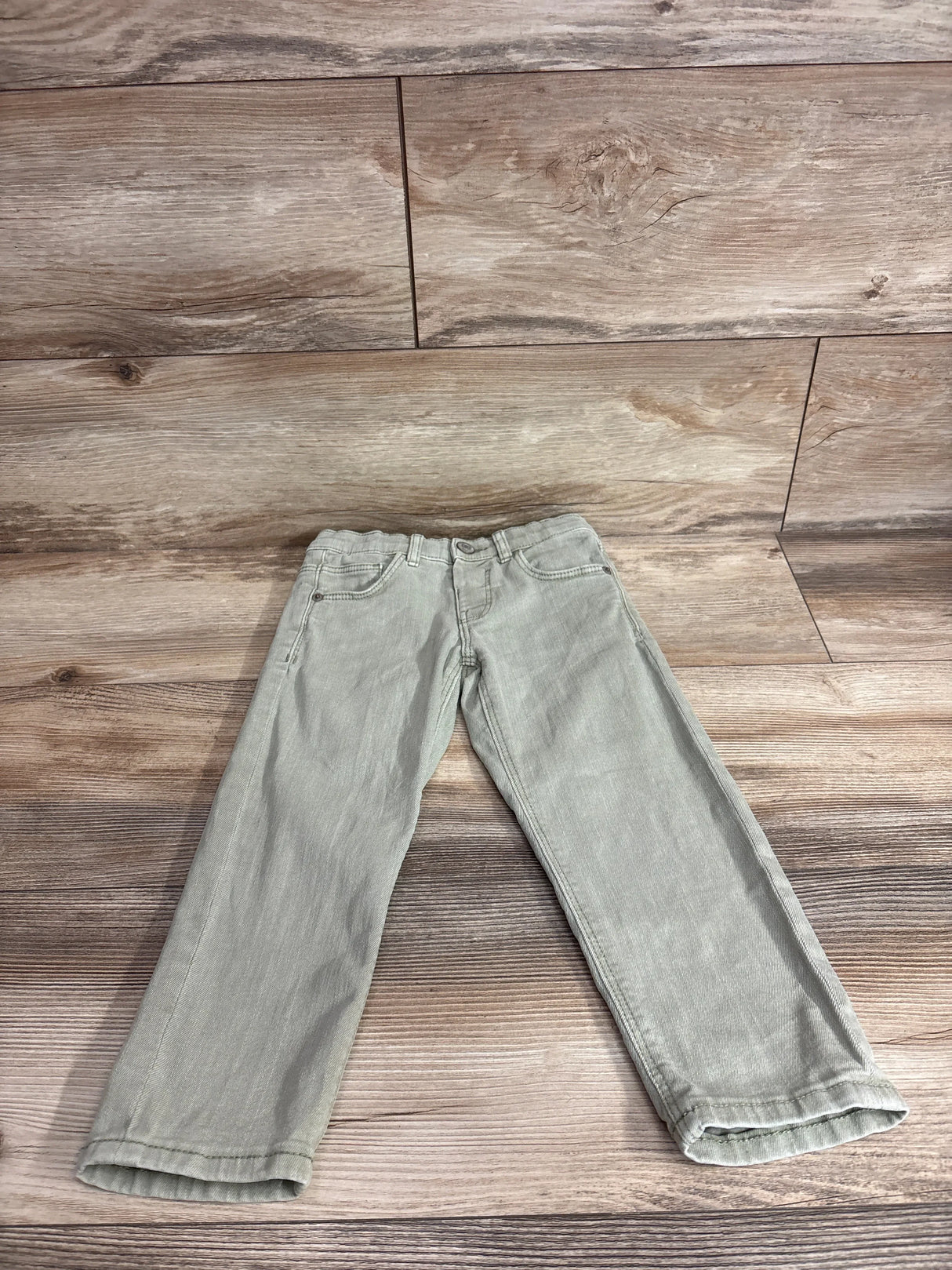 Flat lay of Zara The Regular denim jeans, green (4T), straight legs, five pockets and adjustable waist on wood floor