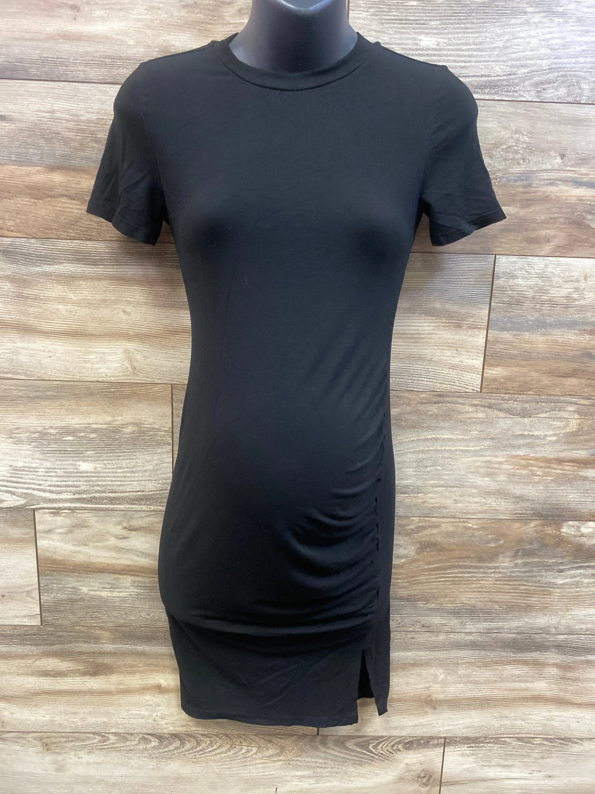 Front view of Shein black maternity dress showcasing short sleeves, ruched side, and hem slit on wood backdrop