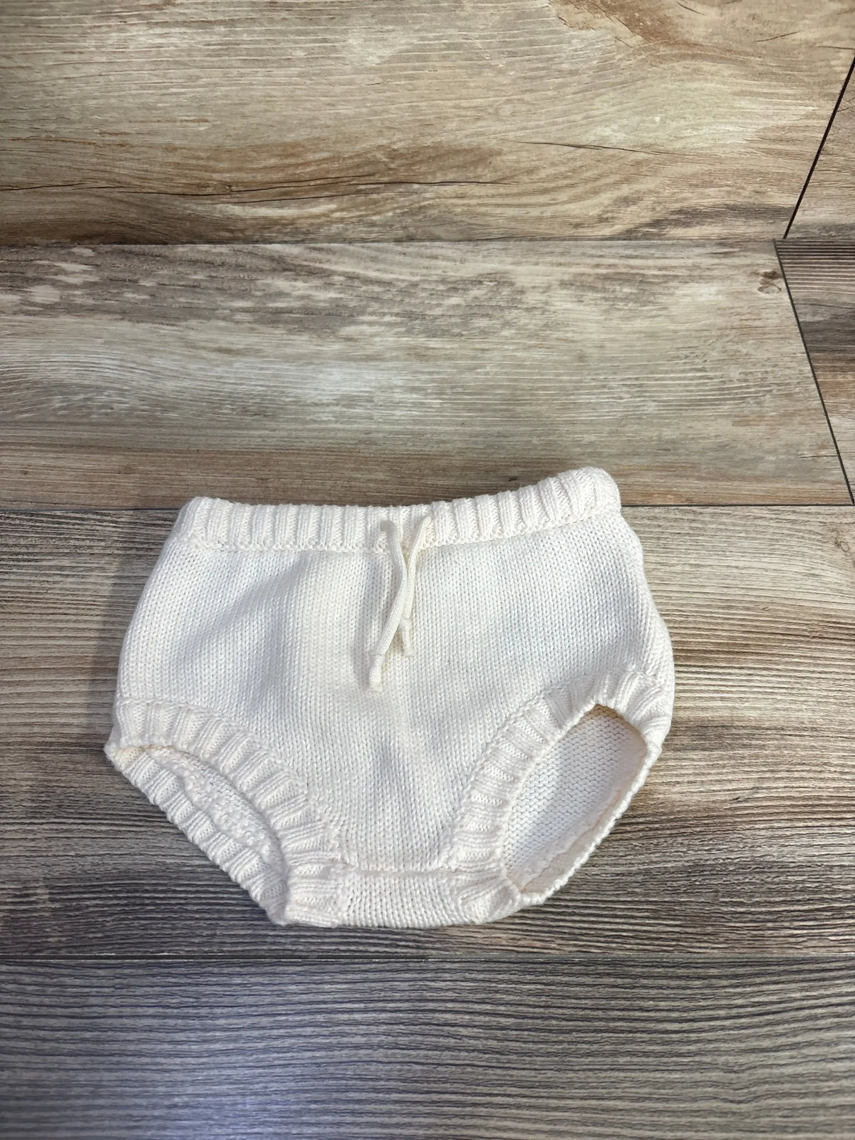 Front view of Little Navy cream organic cotton knit bloomers showcasing ribbed trim and drawstring on a wood-grain background