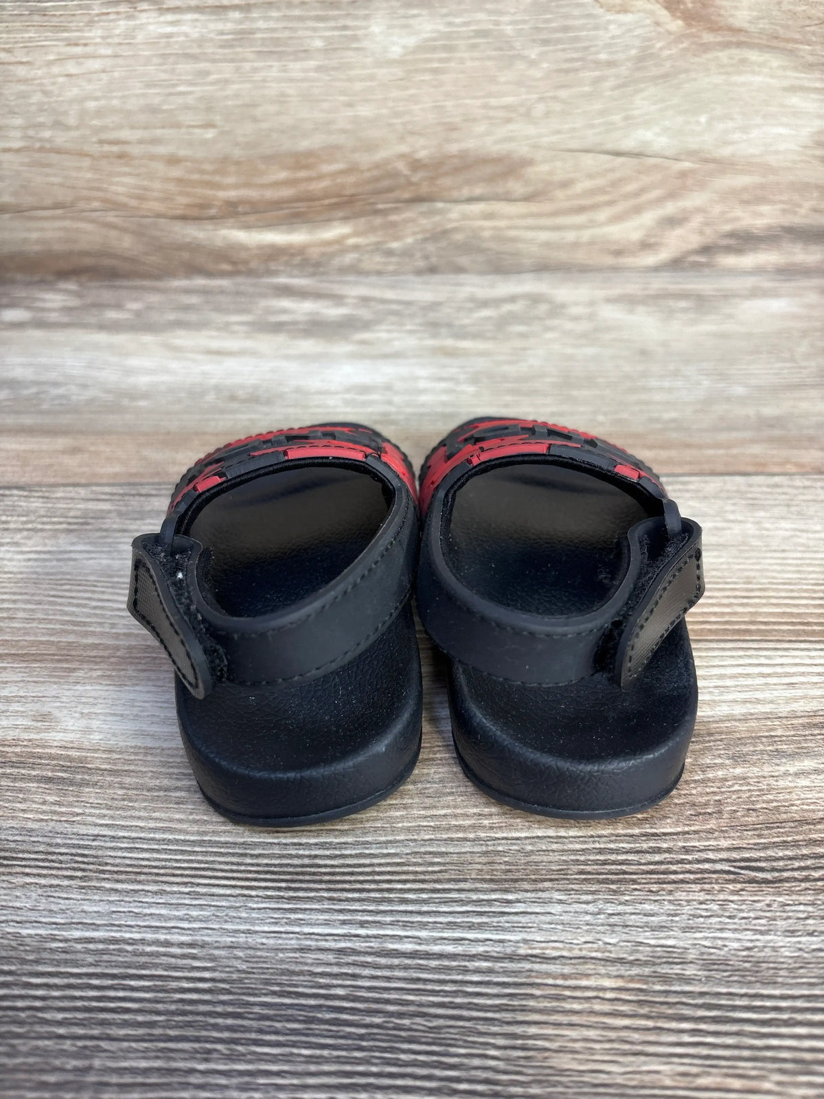 Top view of And1 camo slide sandals showcasing red camouflage accents and black footbeds on a wood-grain surface