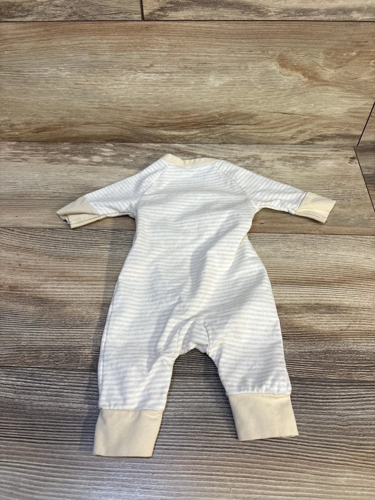Cream and white striped baby onesie with long sleeves, laid flat on wood floor
