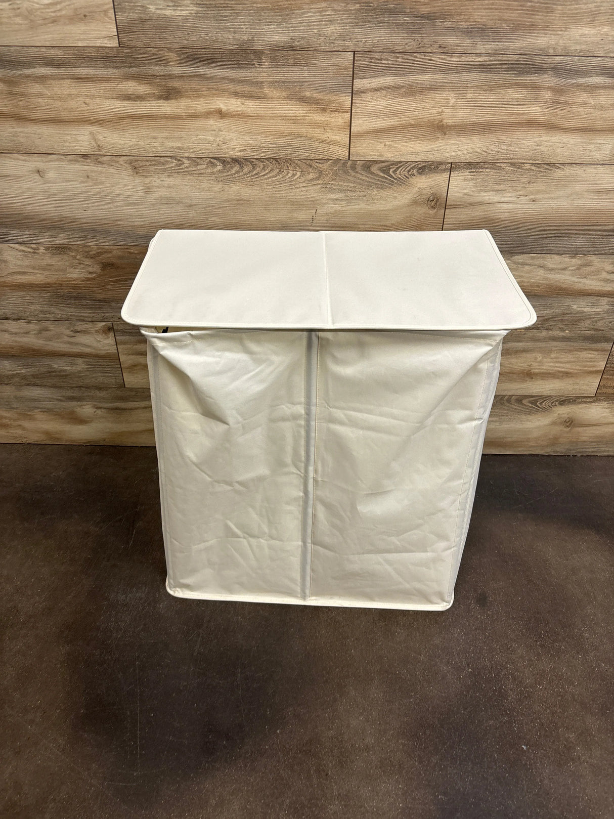 Front view of white double laundry hamper with lid showcasing two fabric compartments against wood plank wall and dark floor