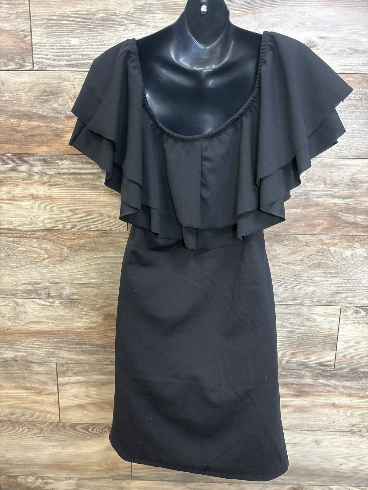 Front view of black My Bump Ruffle Off The Shoulder Dress in XL showcasing layered ruffle sleeves on wood-look floor