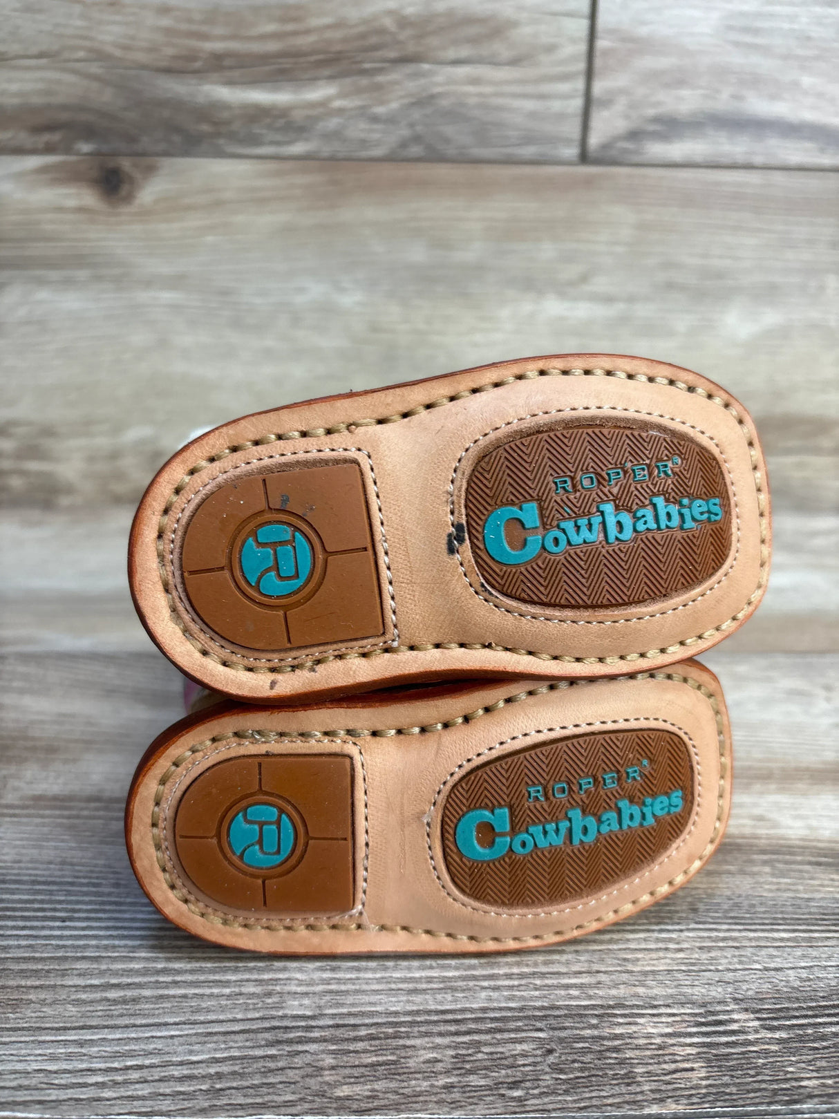 Roper Cowbabies infant cowboy boots with tan soles and turquoise logo on wood background