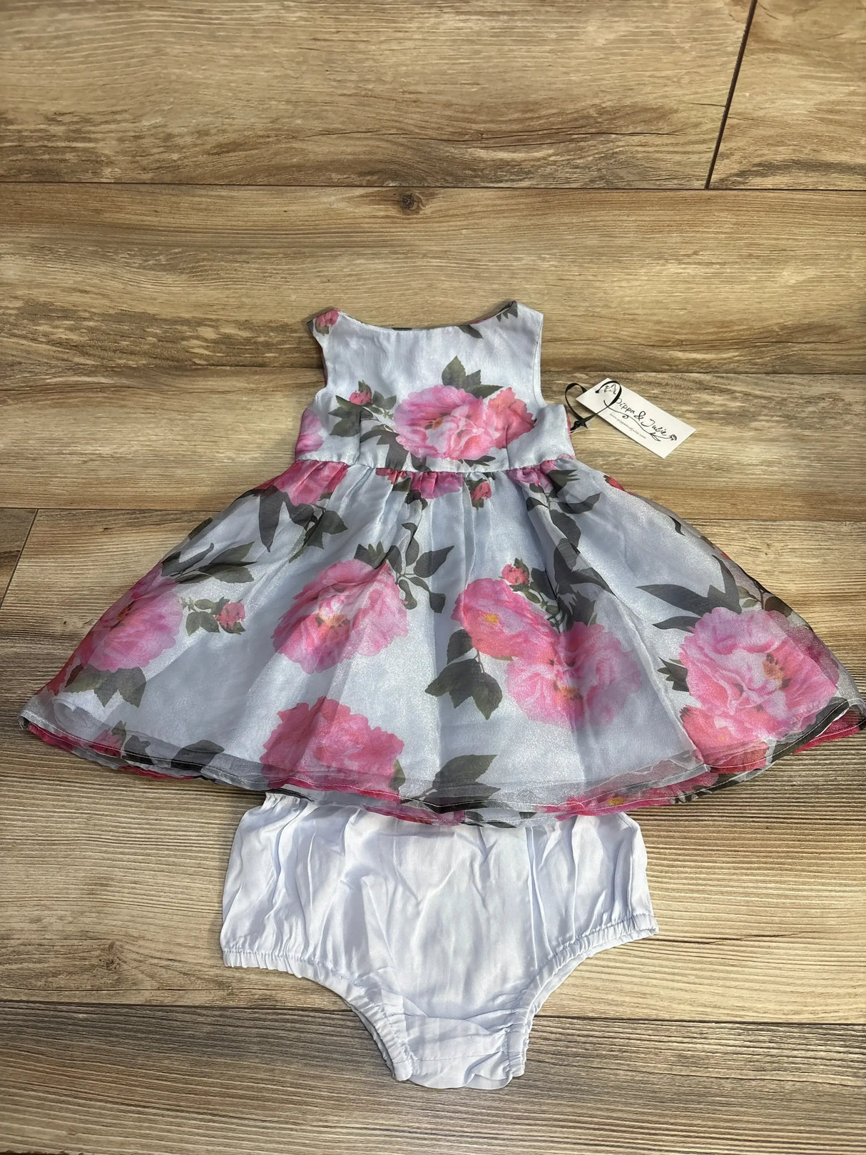 Flat lay of Pippa and Julie 2-piece floral dress with pink roses and matching white bloomers, size 24M on wood floor