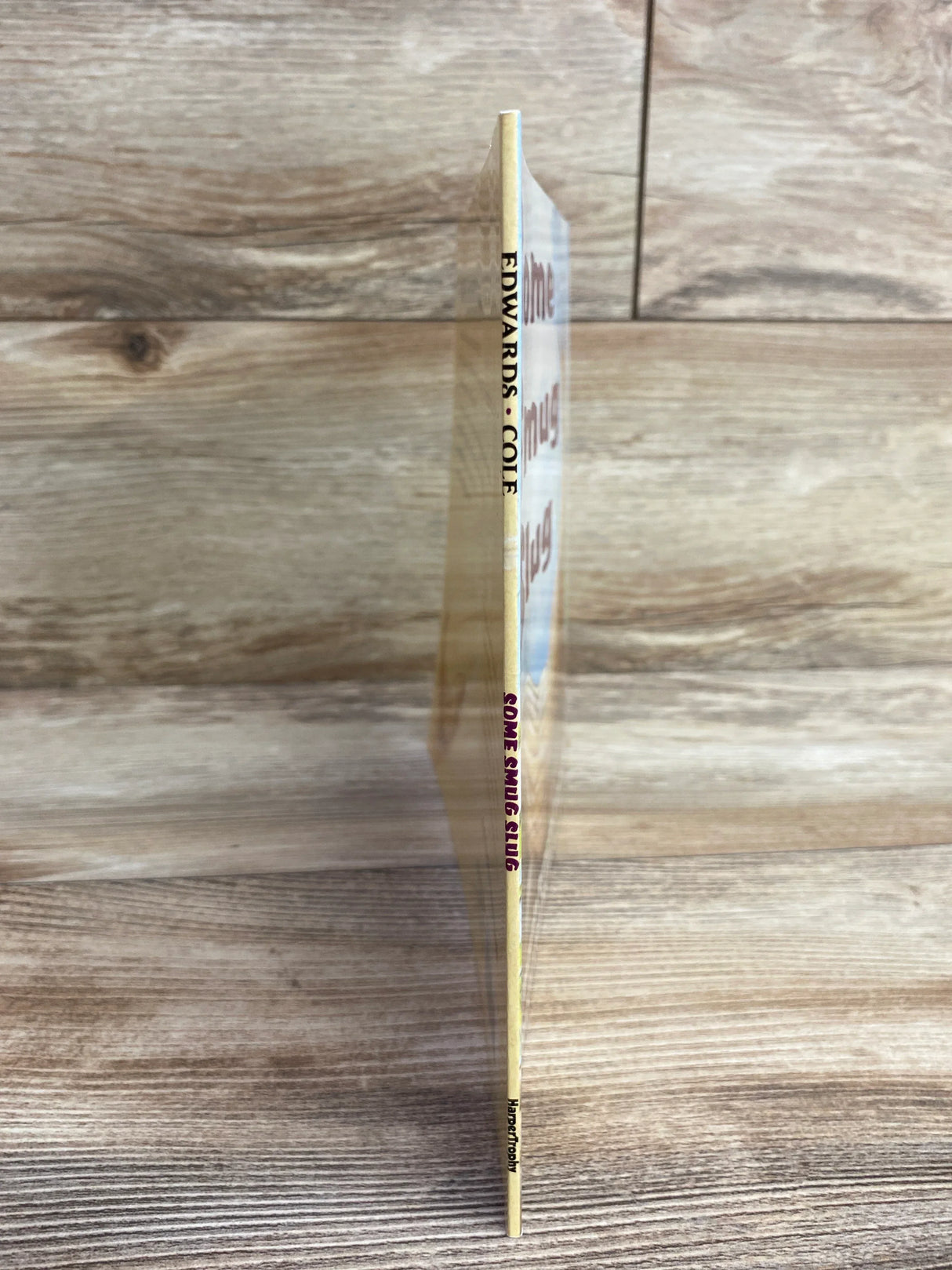 Side view of Some Smug Slug paperback book showing thin spine with title and author name against wood background