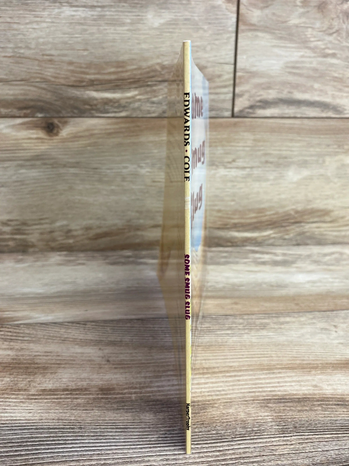 Side view of Some Smug Slug paperback book showing thin spine with title and author name against wood background