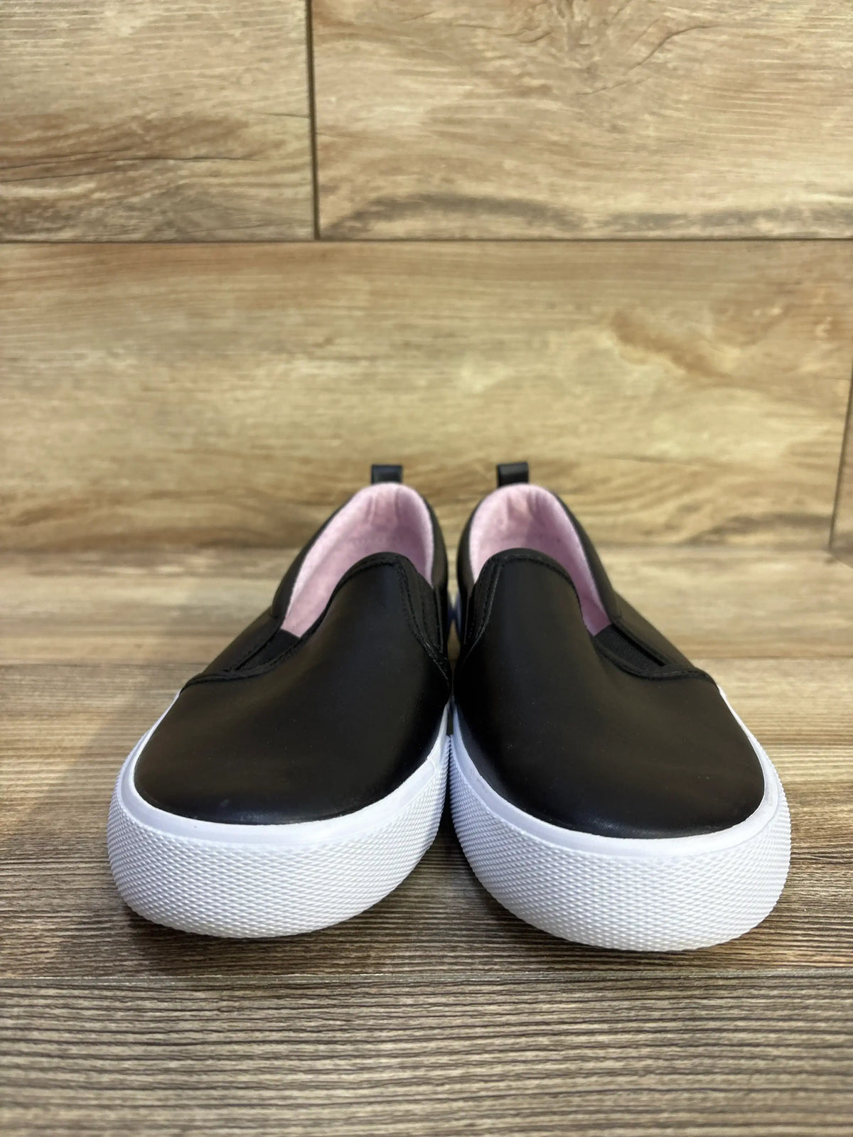 Front view of Cat & Jack Hailey slip-on sneakers showing black upper, white platform sole and pink lining on wood background