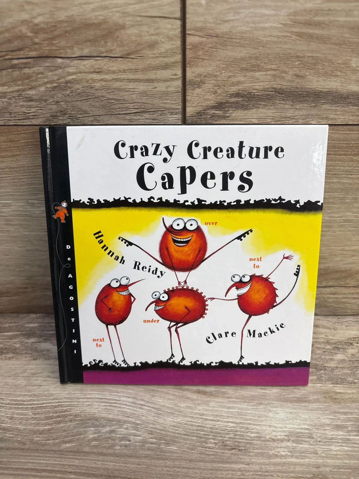 Front cover of Crazy Creature Capers hardcover book showing bug-eyed creatures demonstrating prepositions on a wood floor
