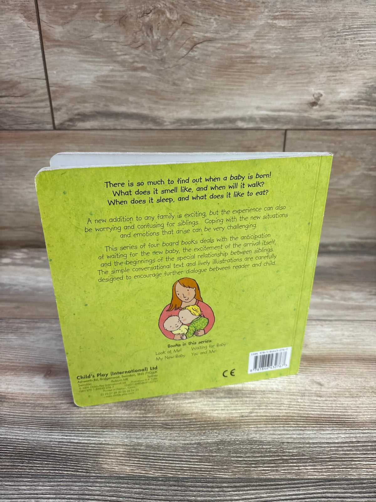 Back cover of My New Baby board book showcasing green cover, back-cover text, and mother with two babies on wood background