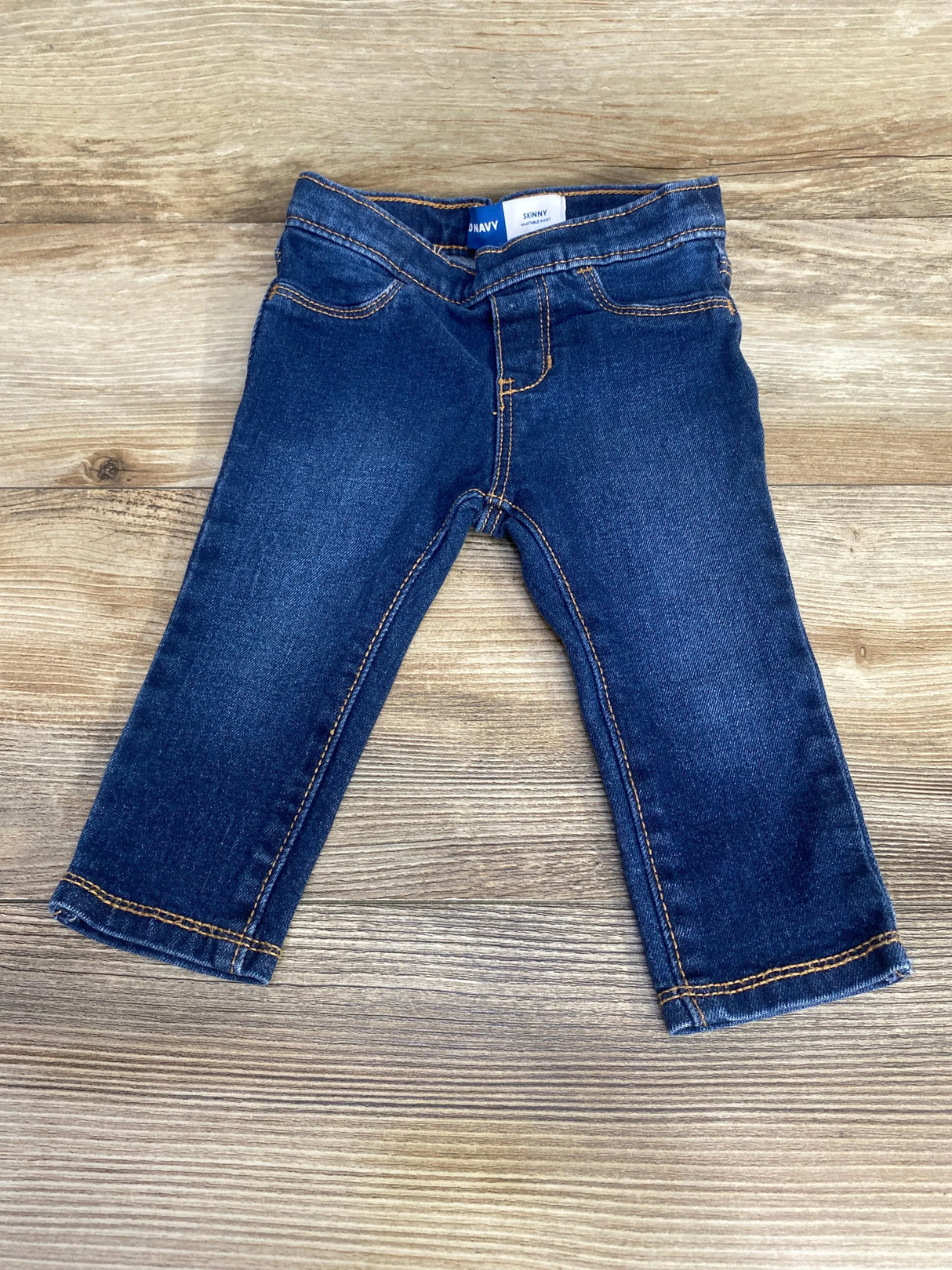 Flat lay of Old Navy toddler skinny blue jeans (size 12 to 18 months) showcasing elastic waist and contrast orange stitching on light wood background