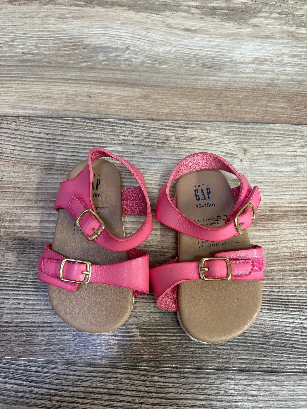 Top down view of Baby Gap pink toddler buckle sandals showing two adjustable gold buckles and tan footbeds on wood floor
