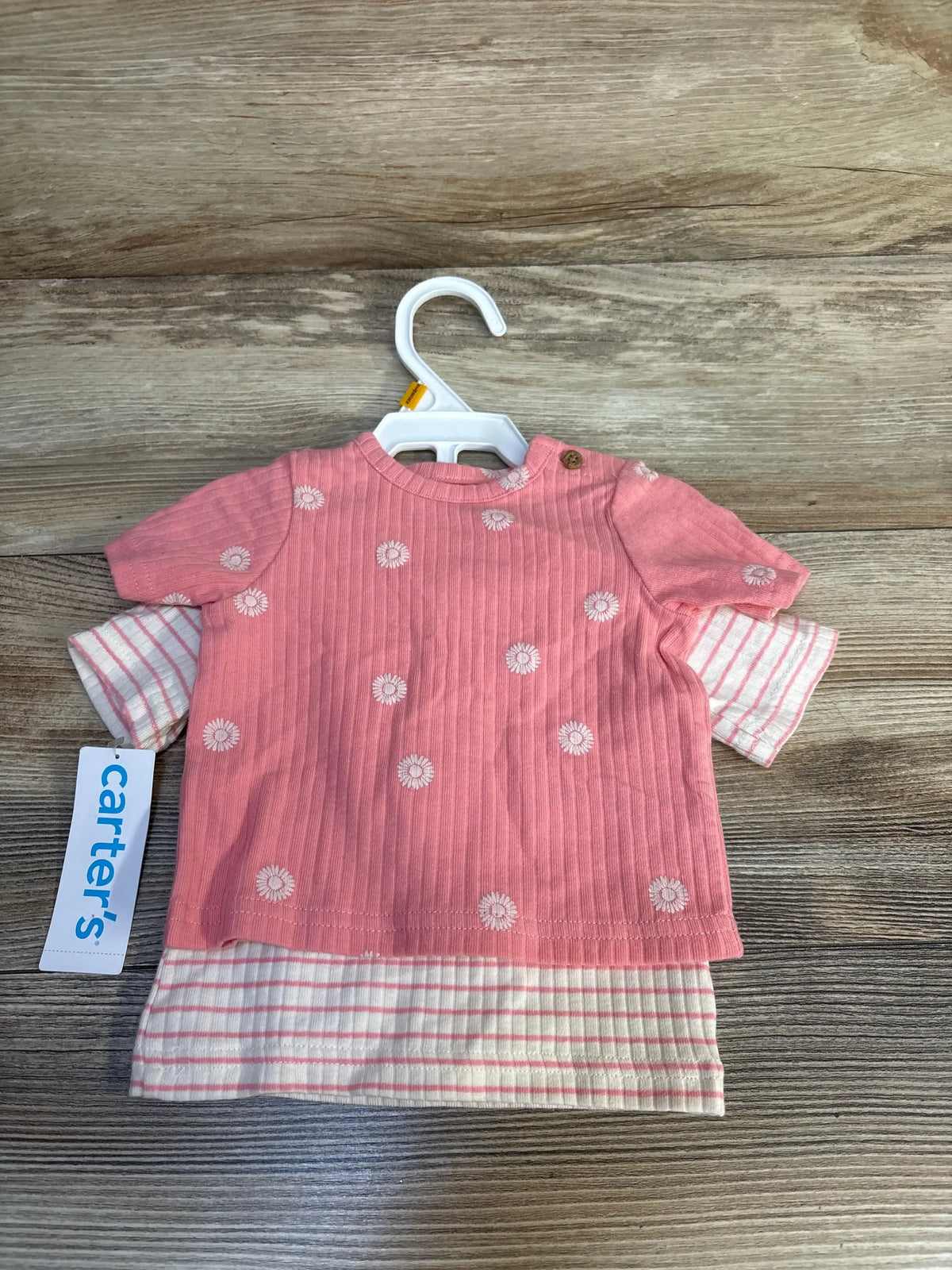 Pink baby short sleeve top with white daisy print and striped underlayer on wood surface