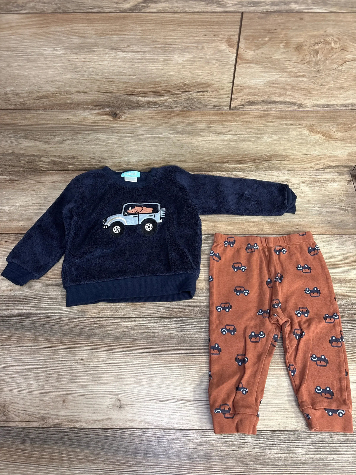 Children's navy blue fleece sweatshirt with car and animal design paired with orange pants featuring car print on wooden floor