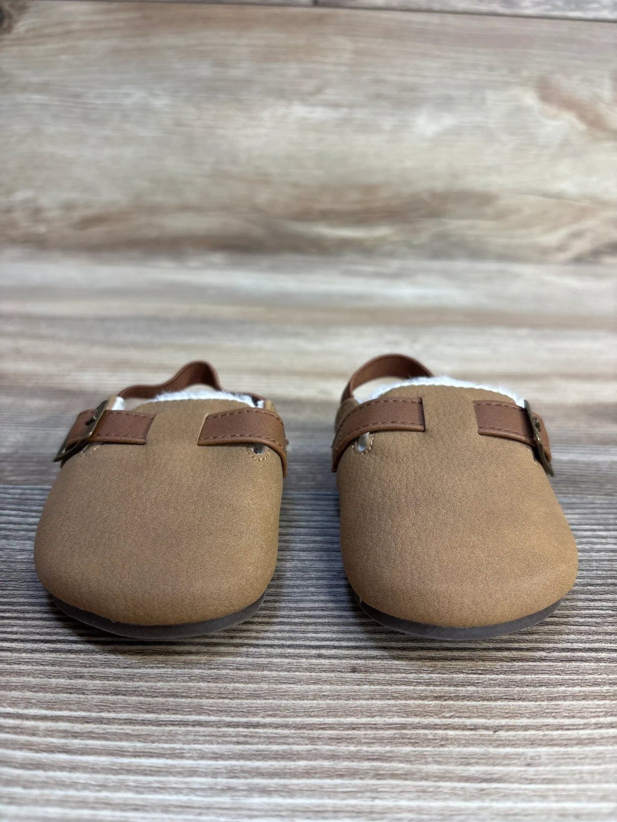Tan toddler moccasins with brown straps and buckles on wood background