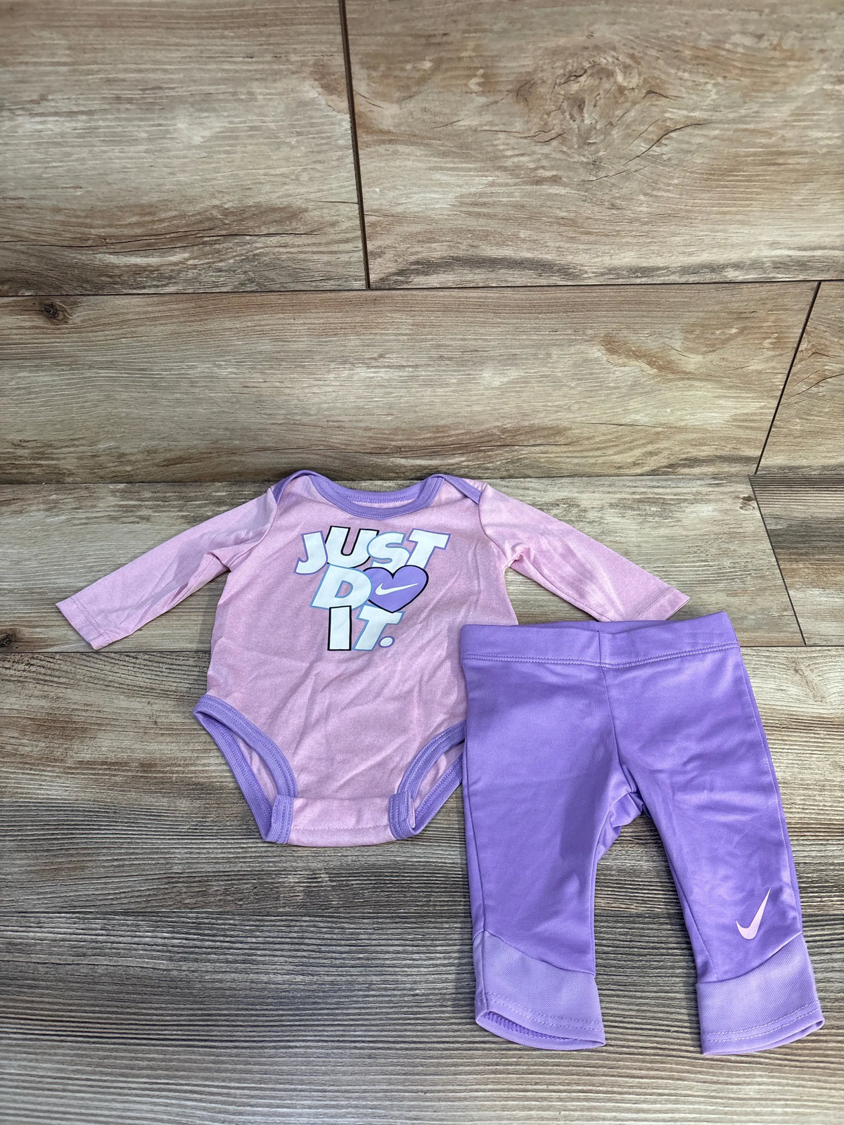 Top view of Nike two-piece bodysuit and pants set showcasing pink colors and Just Do It graphic on wood floor