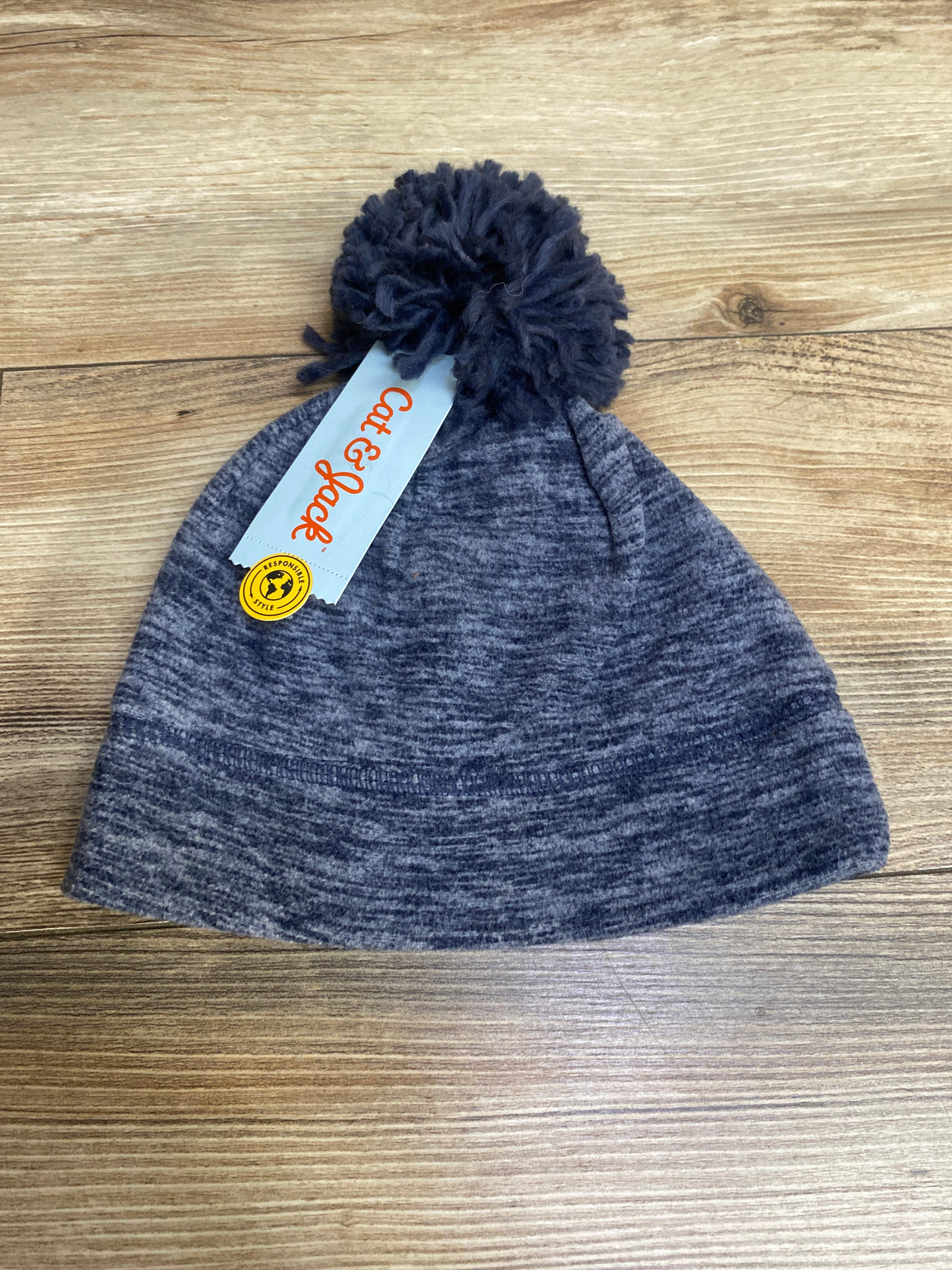 Gray knitted beanie hat with pom-pom and Cat & Jack tag on wooden surface