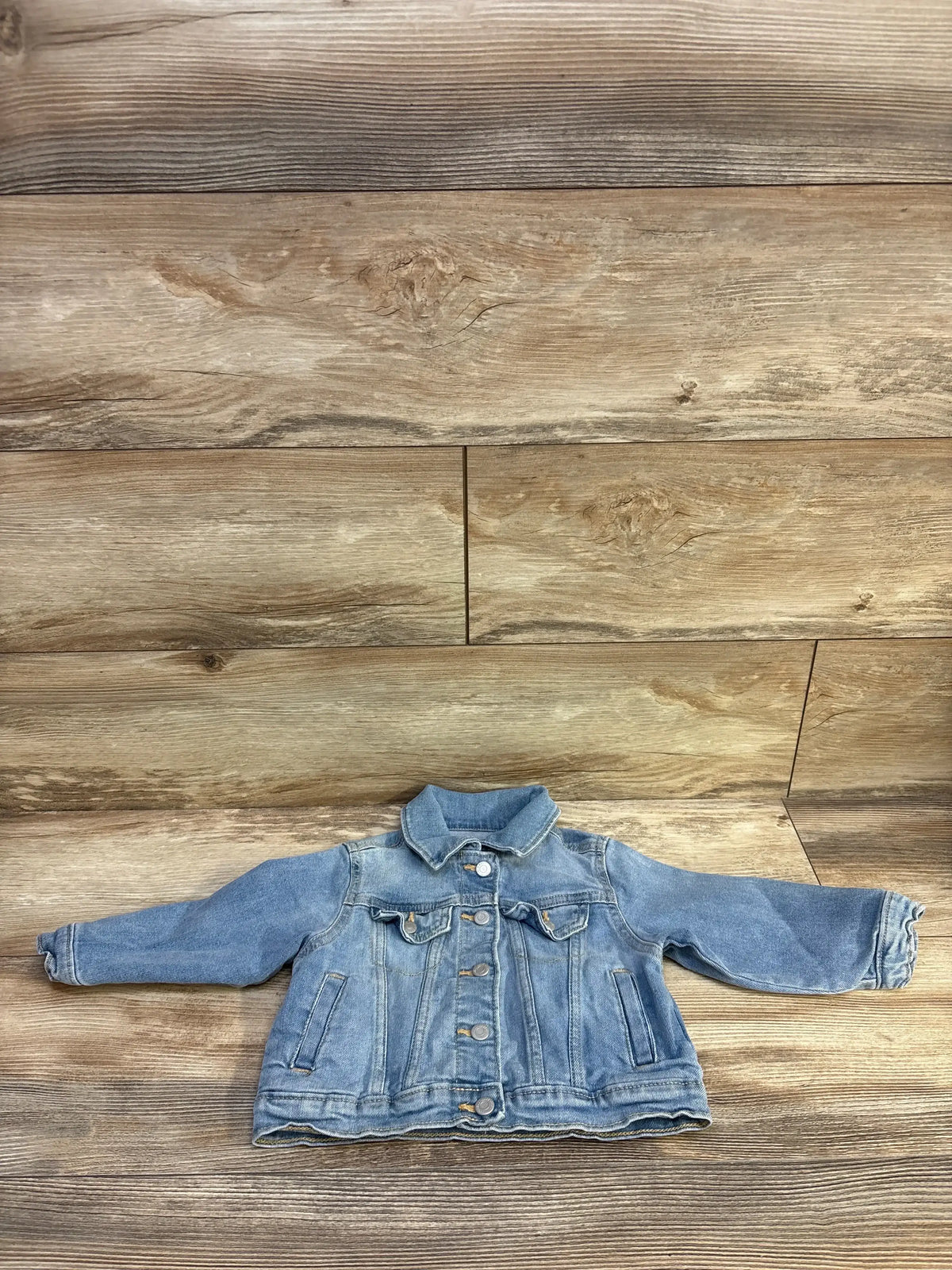 Flat lay of Old Navy toddler denim jacket showing button front, chest flap pockets, and long sleeves on wood background