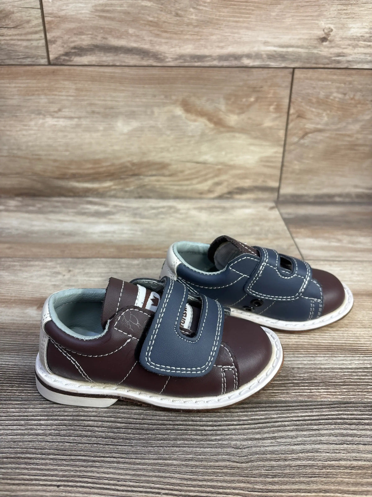 Three-quarter view of Brunswick bowling shoes showcasing the brown colorway and hook and loop closures on a wood-look floor
