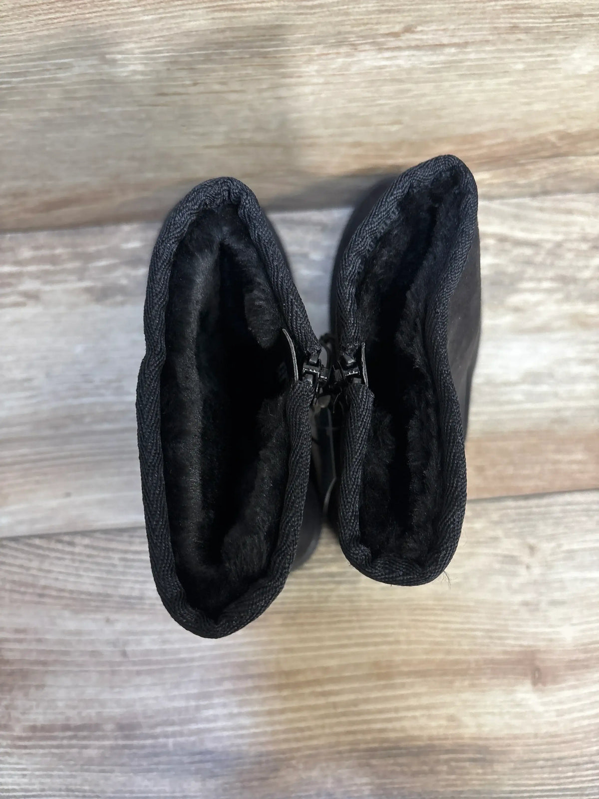 Pair of black fur-lined toddler boots with zippers on wood floor