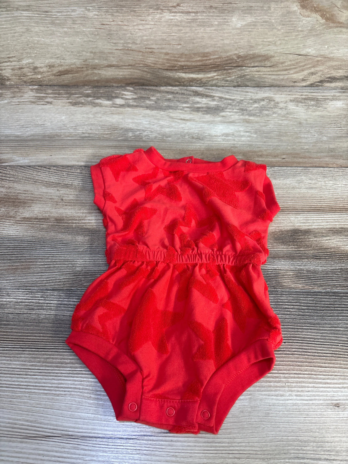 Top-down view of red Cat and Jack terry star romper 0-3M with sleeves, elastic waist and three snap closures on wood floor