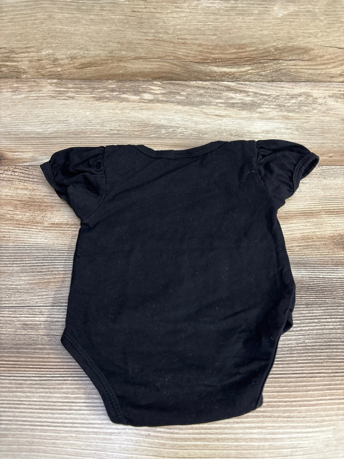 Flat lay of black Hocus Pocus bodysuit in size 0-3m showcasing puff sleeves on a wood-look background